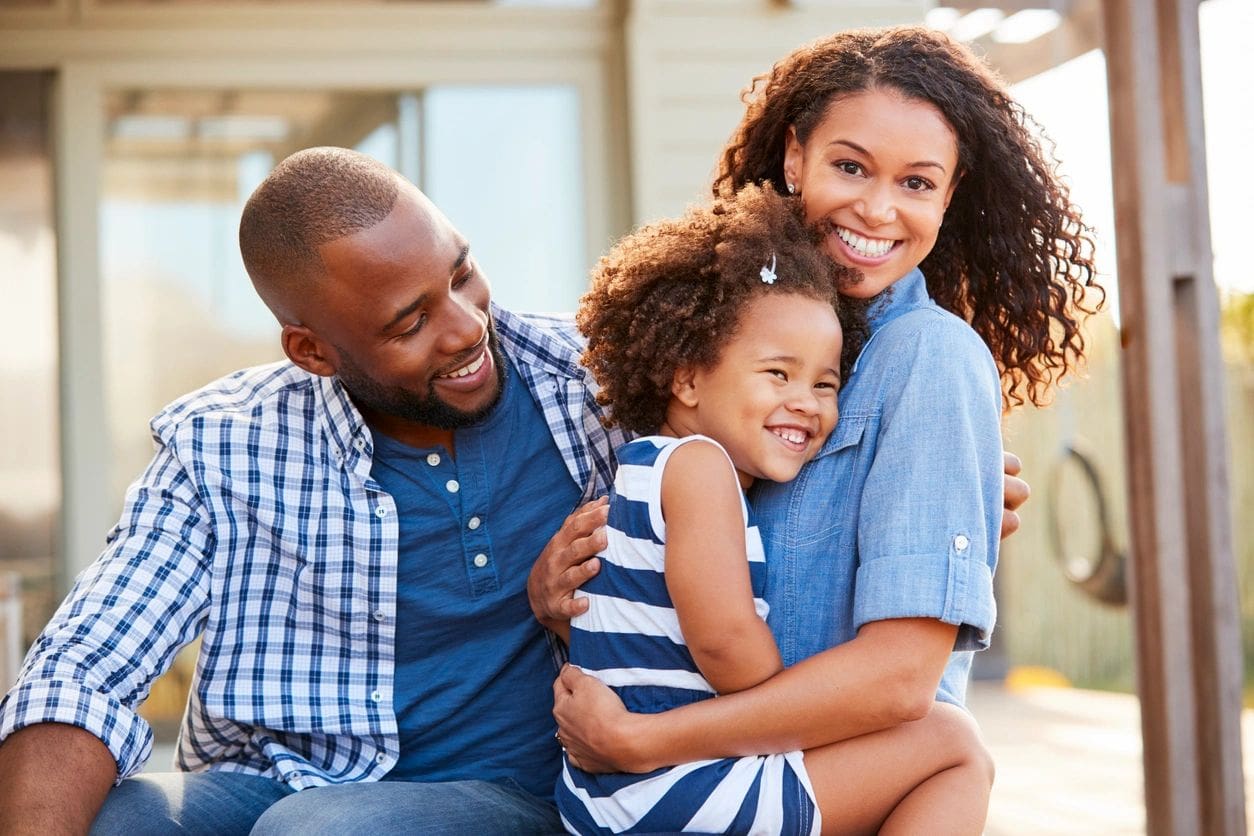 A man and woman hug their daughter while sitting on the ground.