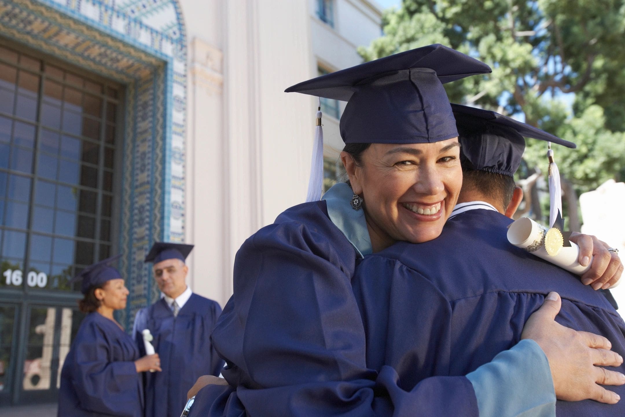 A woman in graduation cap and gown hugging another person.