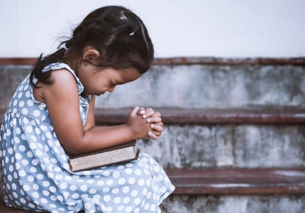 A little girl sitting on the steps holding her hands together.